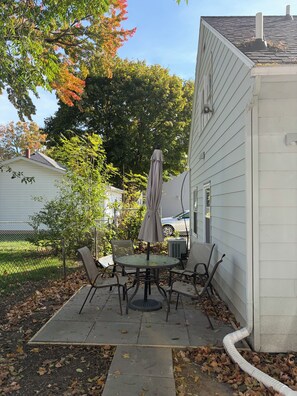 Un patio con una mesa y sillas, una sombrilla y un edificio blanco al fondo.
