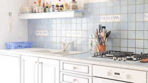 Una cocina con encimera blanca, un fregadero, una estufa y una repisa con diversos utensilios de cocina.