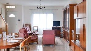 Un comedor con una mesa de madera dispuesta para cuatro personas, rodeada de sillas acolchadas. Un televisor está montado en la pared a la derecha.