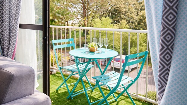 A balcony with a round table and chairs, a small plant, and two glasses.
