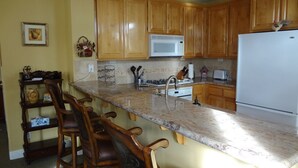 A kitchen with wooden cabinets, a white microwave, a white refrigerator, and a marble countertop.