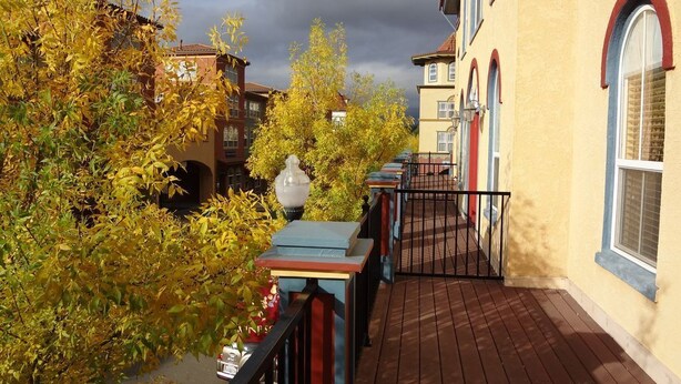 A wooden deck with a railing, a street lamp, and buildings with arched windows and balconies.
