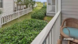 A balcony with a wicker chair, a white fence, and a view of a building with a balcony. -  Cherry Grove Beach Oceanfront 
Finestere -F1 (North Myrtle Beach)