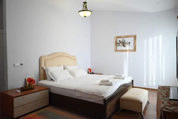 A neatly arranged bedroom with a bed, bedside tables, a nightstand, a chair, and a window with blinds. - Neo Classic Villa: Garden, Playground & Biodesign Pool (tirane)
