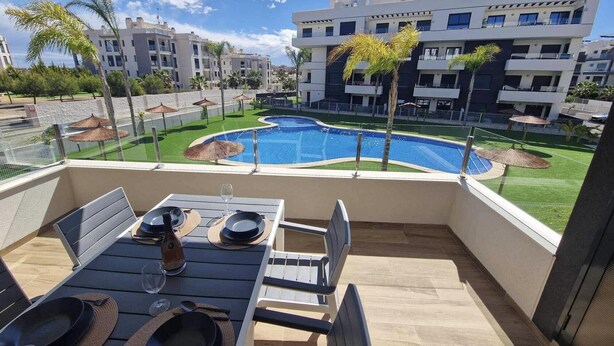 Un balcon avec une table dressée pour le dîner, donnant sur une piscine et des immeubles d’appartements modernes.