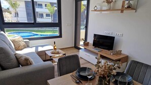 Un salon moderne avec un canapé, une table à manger pour deux personnes, un téléviseur et une vue sur une piscine.