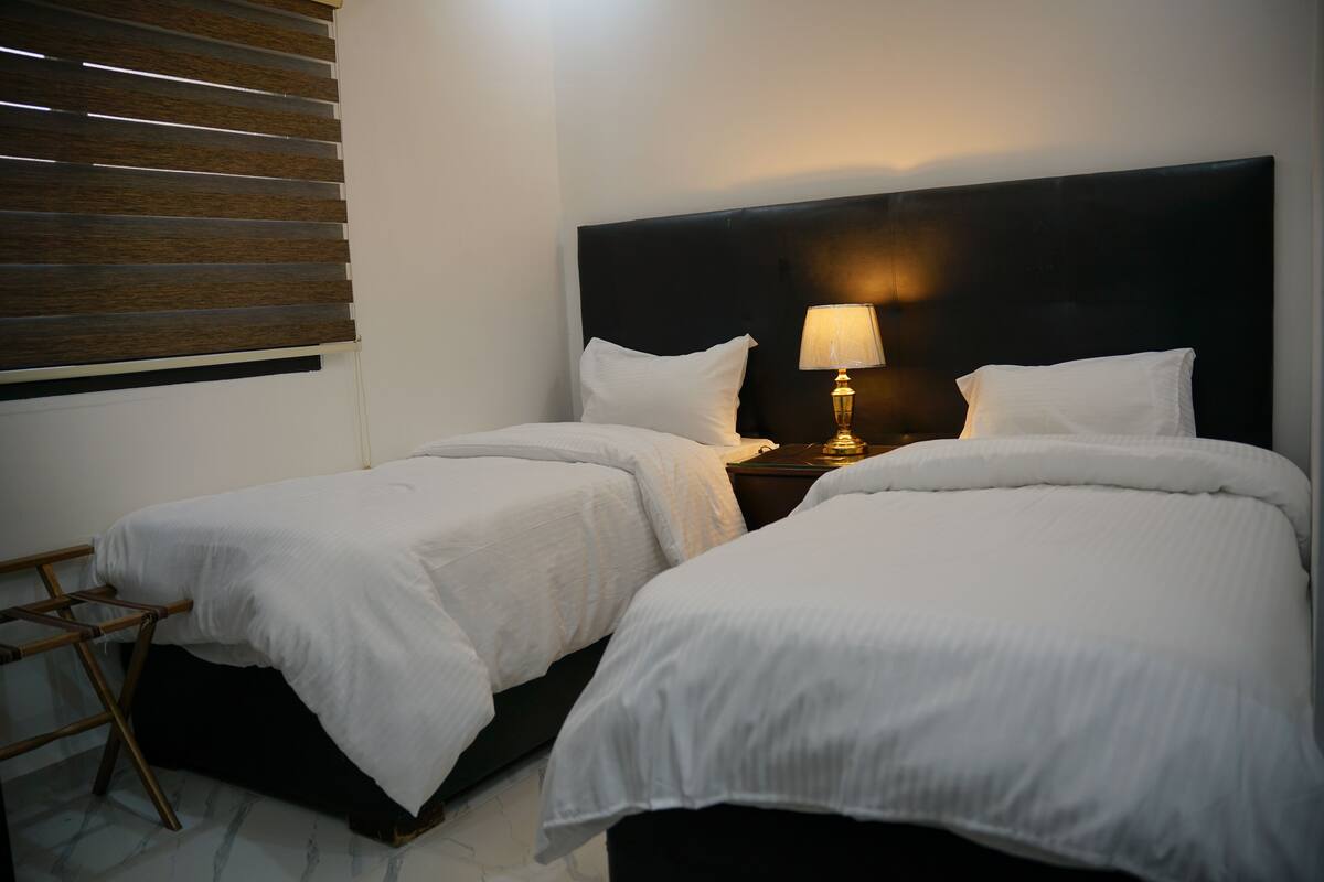 Une chambre d’hôtel avec deux lits simples, une table de chevet avec une lampe et une échelle en bois.