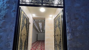 Un couloir avec des portes décorées et un tapis rouge menant à une pièce dont le plafond est également décoré.
