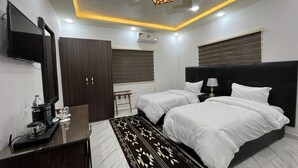 Une chambre d’hôtel moderne dotée de deux lits, d’un téléviseur à écran plat, d’un bureau avec une machine à café et d’un tapis à motifs.