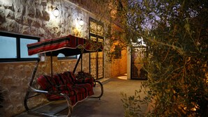 Un espace extérieur aménagé avec des murs en pierre, comprenant un fauteuil suspendu et un banc, tous deux dotés de coussins à rayures rouges et noires.