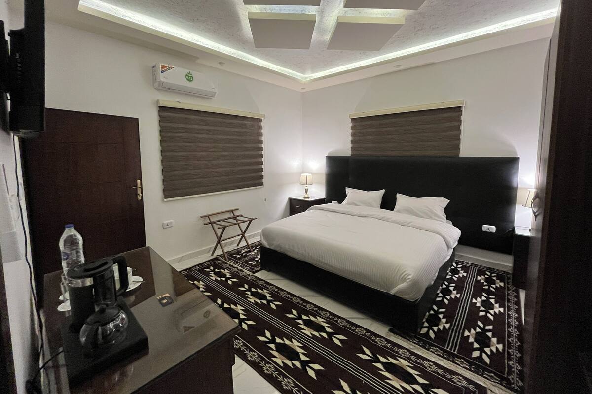 Une chambre d’hôtel avec un lit, des tables de chevet, une bouteille d’eau, une bouilloire et un tapis à motifs.