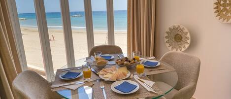 A dining table with plates, cutlery, and glasses, overlooking a beach.