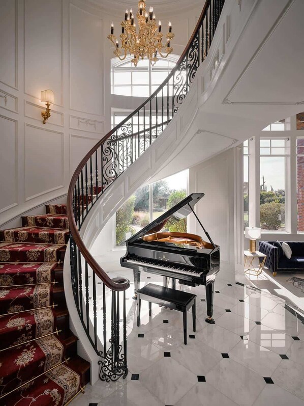 Un interior imponente con una escalera espiral, un piano de cola y una araña de cristal.