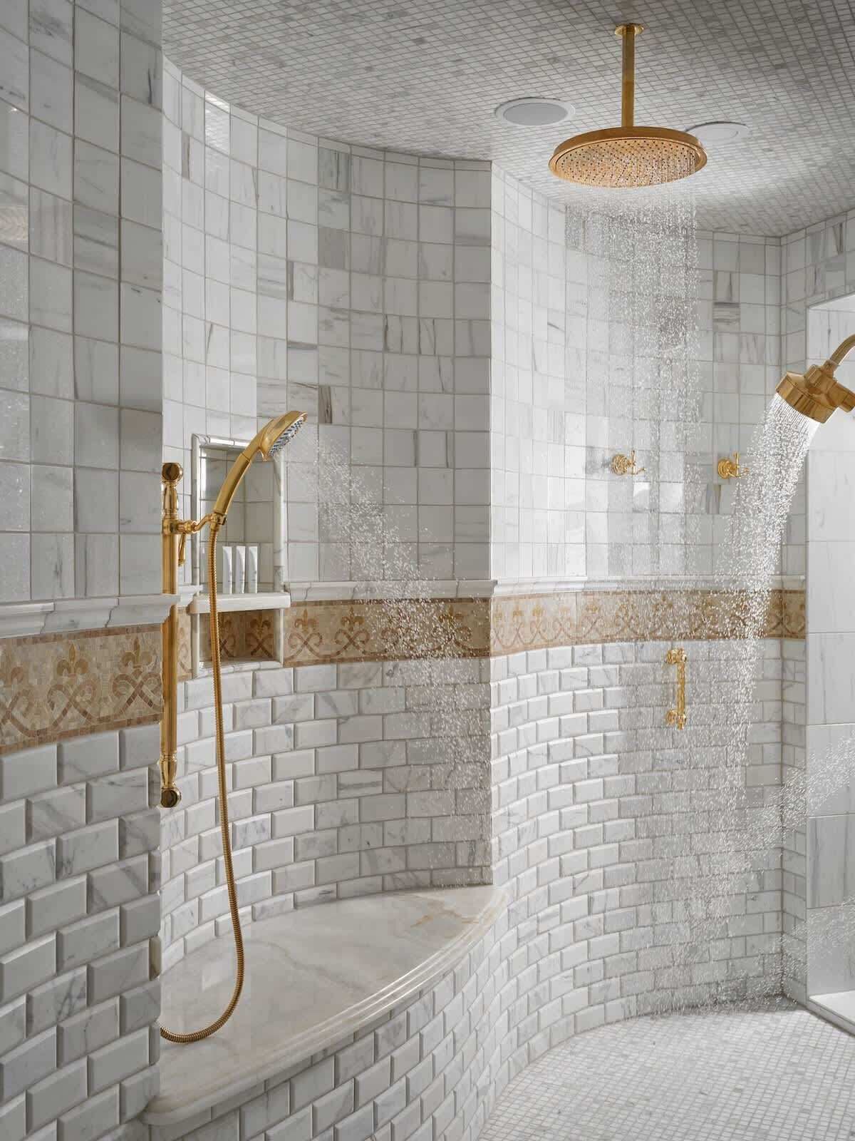 A modern shower area with a curved design, white tiled walls, and a gold showerhead.