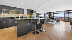 Une cuisine moderne dotée d’un grand îlot central, de meubles de rangement aux couleurs sombres et offrant une vue sur l’extérieur.