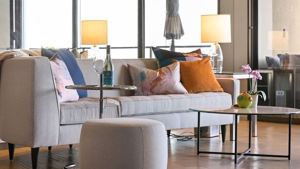 A modern living room with a grey sofa, colorful cushions, a glass coffee table, and a small side table with a bottle and a lamp. - Gorgeous Luxury Highrise w/Spectacular Marina & Ocean Views (Marina Del Rey)