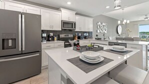 A modern kitchen with white cabinetry, stainless steel appliances, and a central island with seating.