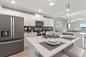 A modern kitchen with white cabinetry, stainless steel appliances, and a central island with seating.