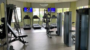 Une salle de sport équipée de tapis de course, d’appareils de musculation et d’un écran de télévision.