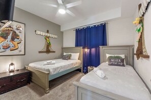 Ein Schlafzimmer mit zwei Betten, einem Deckenventilator, einem Gemälde und einem Fenster mit Vorhängen.