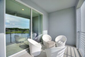 Un balcon avec des chaises blanches et une porte vitrée donnant sur une terrasse d’où l’on peut admirer un paysage verdoyant.
