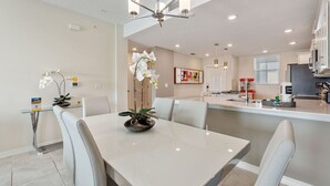 A modern kitchen with white cabinets, a central island, and a dining area with a white table and chairs.