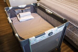 A portable crib with a mattress and folded blankets, placed near a bed with a patterned bedspread. - 15103 Resort 2BR Condo Apt by Disney World Orlando (Kissimmee)