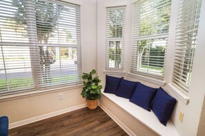 A room with a built-in bench along a window with white blinds, a potted plant, and a wooden floor.