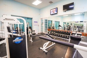 A gym with various exercise equipment, a television mounted on the wall, and a mirror reflecting the equipment.