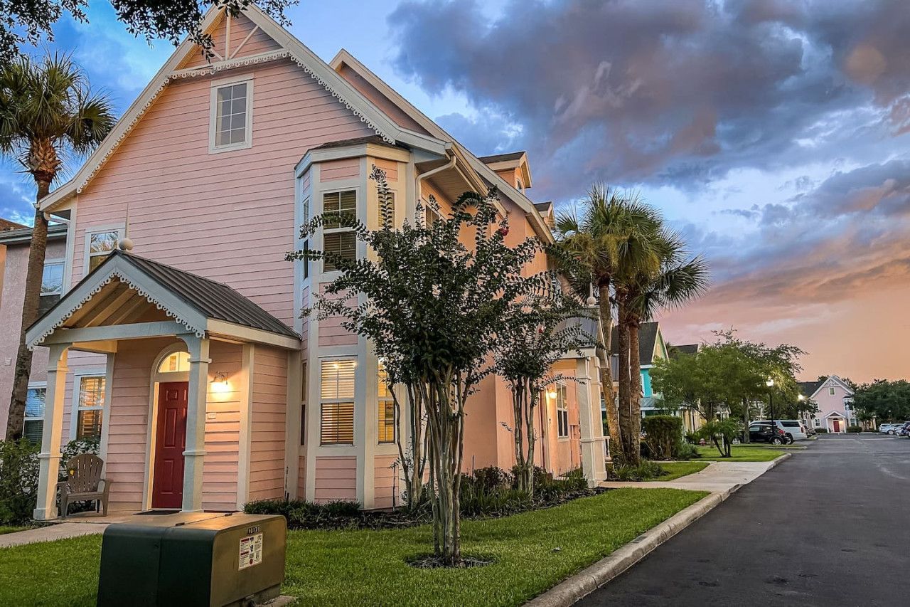 A pink house with a porch and mailbox, surrounded by trees and a street.