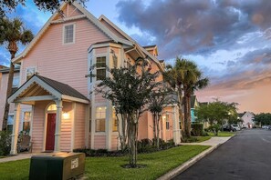 A pink house with a porch and mailbox, surrounded by trees and a street.