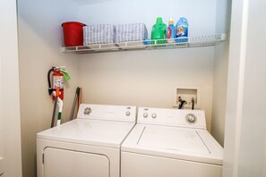 A laundry area with two front-loading washers and a shelf above containing cleaning supplies.