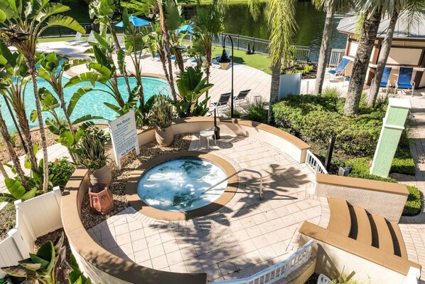 A hot tub surrounded by lounge chairs and a pool, with a sign indicating spa rules.