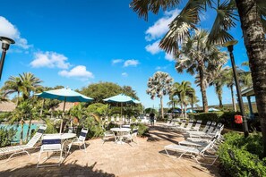 A poolside area with sun loungers, umbrellas, and palm trees. - 15103 Resort 2BR Condo Apt by Disney World Orlando (Kissimmee)