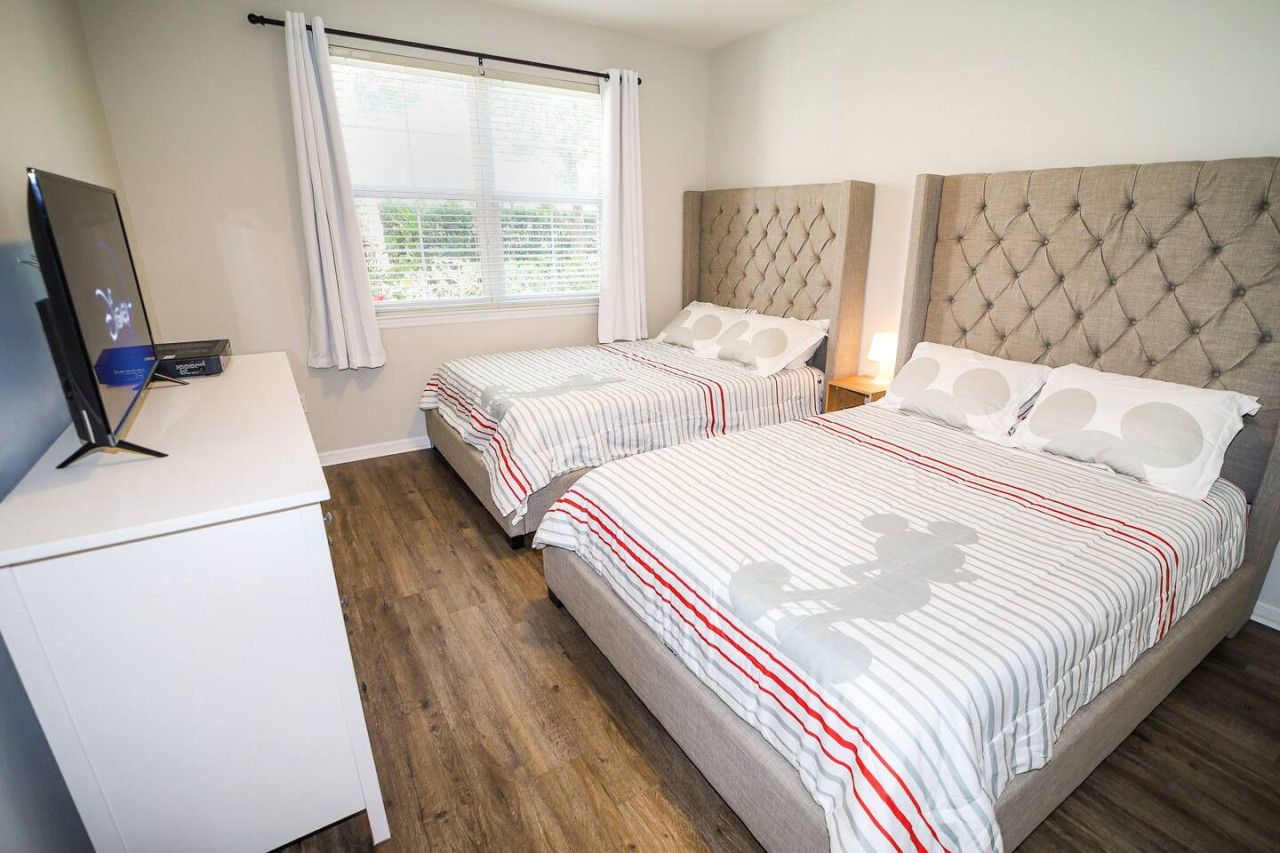Habitación de hotel con dos camas, televisión, escritorio y ventana con cortinas.