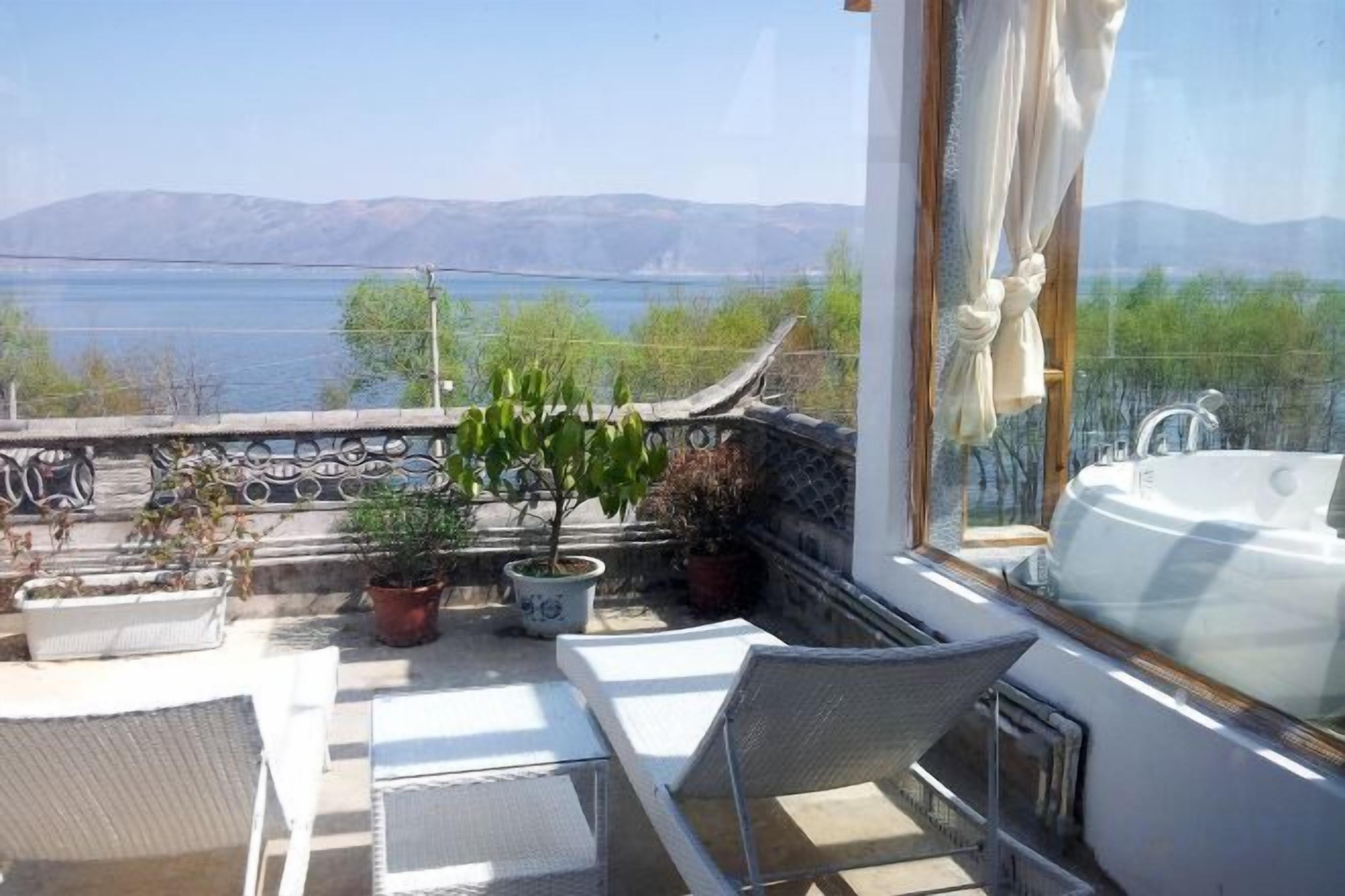 A balcony with a view of a lake and mountains, a white bathtub, and potted plants.