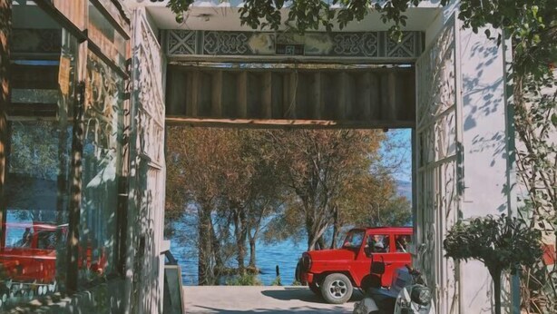 Un coche rojo estacionado bajo una estructura cubierta, con vistas a árboles y agua.
