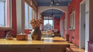 Un pasillo con un banco de madera, un jarrón con flores secas y vista a un edificio a través de un arco.