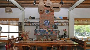 Comedor con una larga mesa de madera y sillas, rodeado de estanterías con libros y objetos decorativos, y una pared de ladrillo con un dardo.
