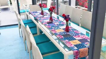 A long dining table with chairs, a patterned tablecloth, and red flowers in vases.