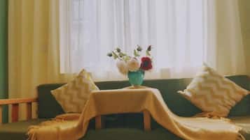 A green sofa with a table and a vase of flowers in front of a window with sheer curtains.