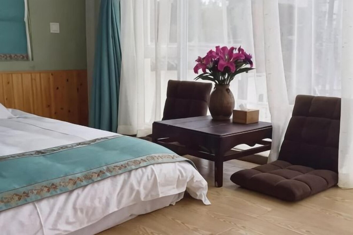 Habitació d'hotel amb un llit, una taula petita amb un vas de flors, dues cadires i una nitòria de fusta.