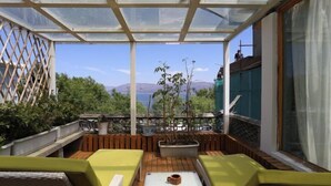 Un espacio al aire libre iluminado por el sol, con bancos de madera y una mesa, con vistas a un paisaje pintoresco con árboles y montañas.