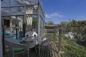 A glass-enclosed outdoor area with a wooden deck, white wicker chairs, and a small table. - Haiyang Lanlan Erhai Garden Sea View Inn (Dali City)