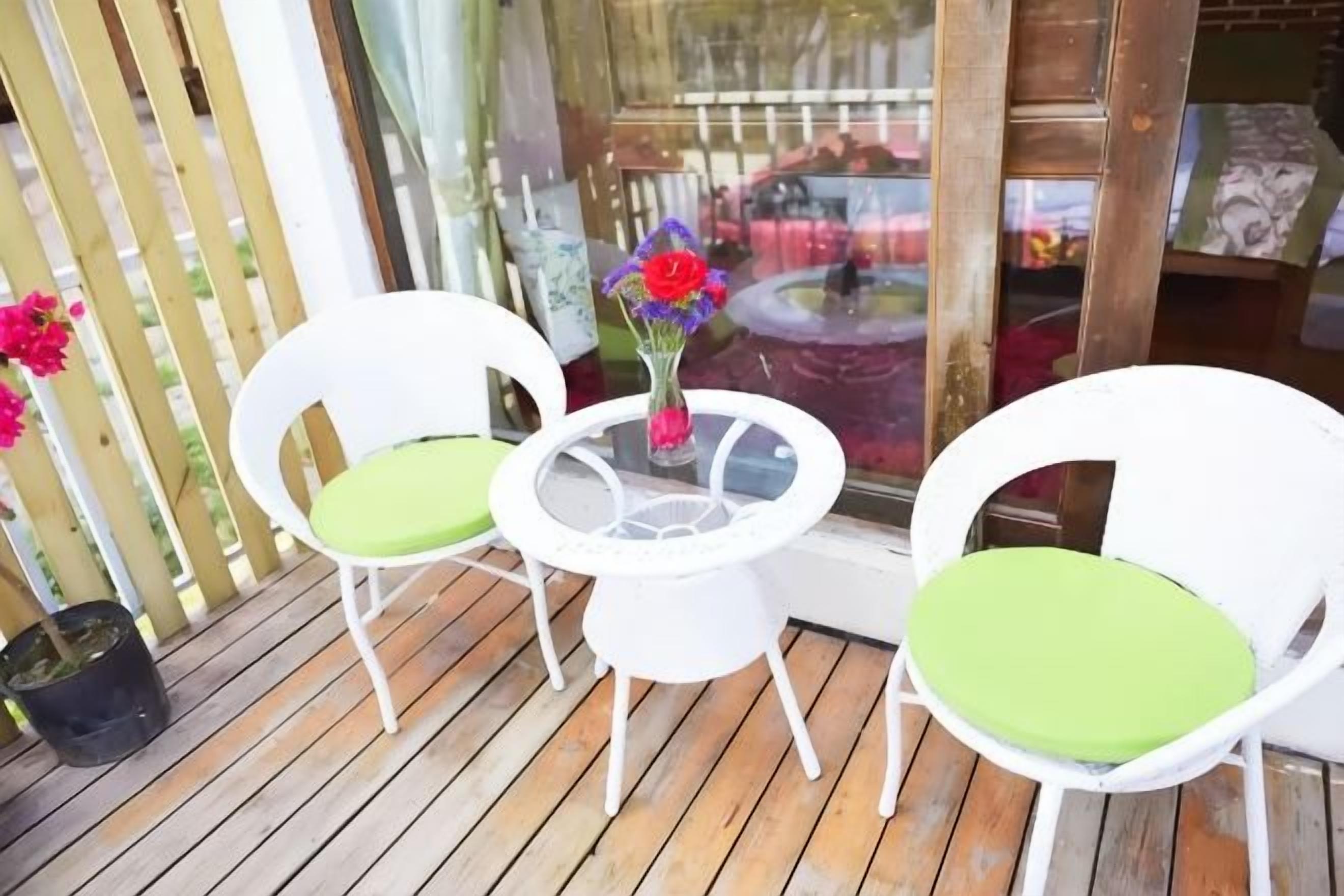 A wooden deck with two white chairs and a small table with a vase of flowers.