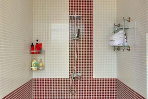 Un baño con ducha, paredes con azulejos y repisas con artículos de aseo.