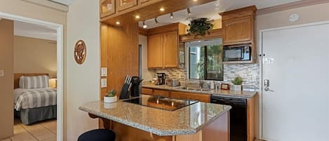 A compact kitchen with wooden cabinets, a granite countertop, and a dishwasher.
