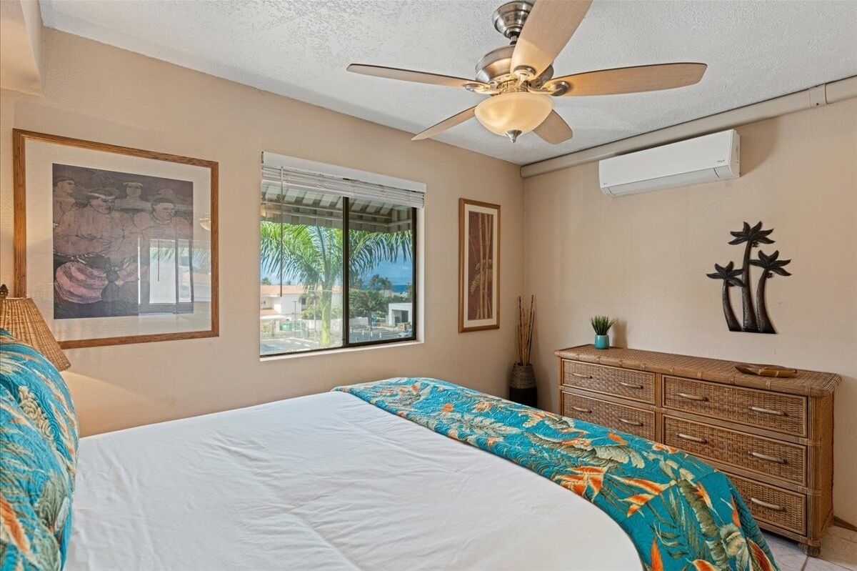 Une chambre à coucher comprenant un lit, un ventilateur de plafond, une fenêtre avec vue, une commode et des œuvres d’art murales.