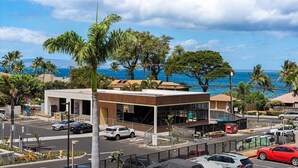 A modern building with a parking lot and a view of the ocean. - Pacific Shores A302 3 Bedroom Condo (Kihei)