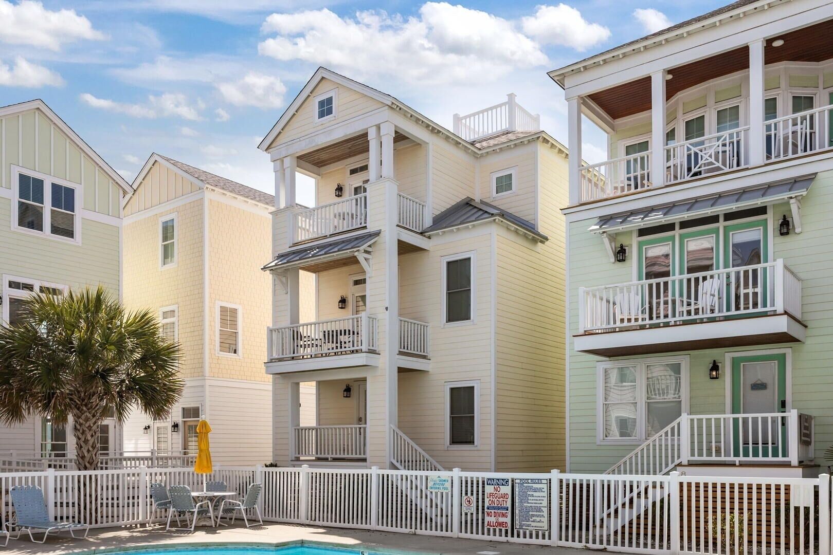 A multi-story residential building with balconies, a swimming pool, and a white picket fence.
